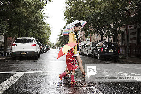 Seitenansicht von Mutter und Tochter  die beim Überqueren der Straße Regenschirme halten