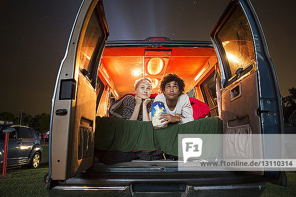 Couple holding popcorn while sitting in camping van during drive-in movie