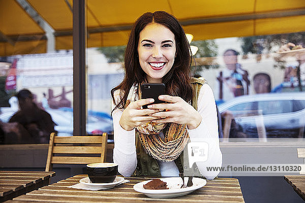 Porträt einer Frau  die ein Mobiltelefon benutzt  während sie in einem Straßencafé sitzt