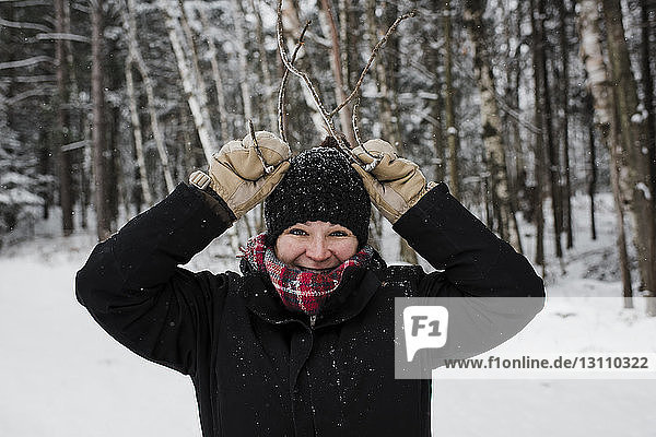 Portrait of smiling woman gesturing while standing in forest during winter
