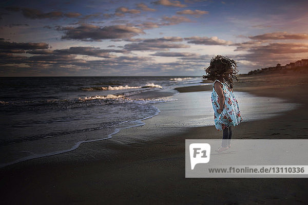 Playful girl jumping at beach against cloudy sky