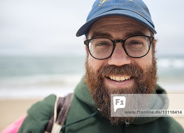 Close-up portrait of smiling bearded man wearing cap and eyeglasses at beach
