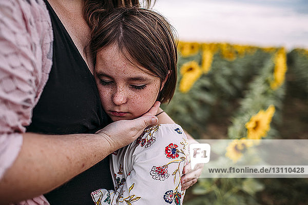 Mittelteil einer Mutter  die ihre Tochter umarmt  während sie in einer Sonnenblumenfarm steht
