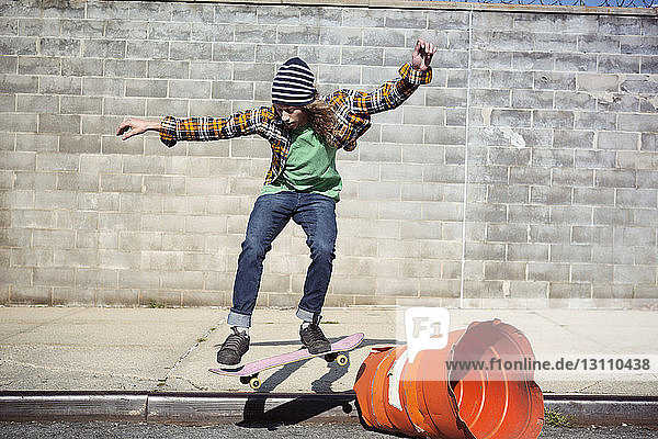 Man performing skateboard stunt over barrel on street