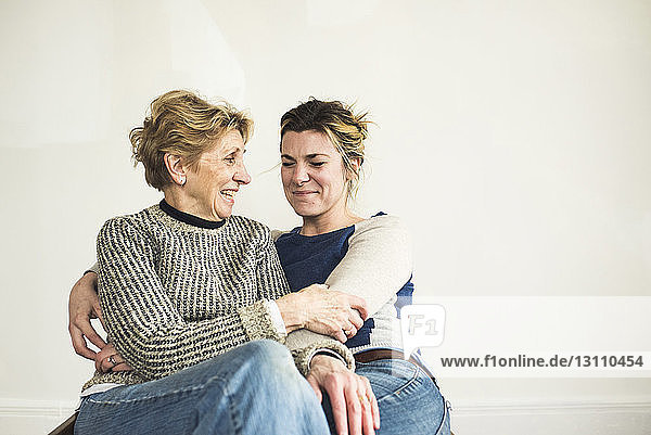 Fröhliche Mutter und Tochter sitzen zu Hause an der weißen Wand