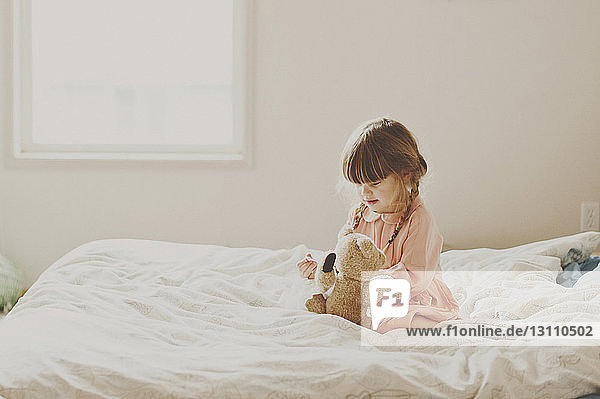 Cute girl playing with teddy bear on bed