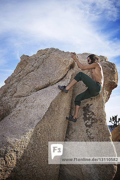Side view of determined man climbing rock against sky