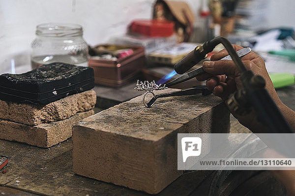 Cropped hands of female artist using blow torch on ring in workshop