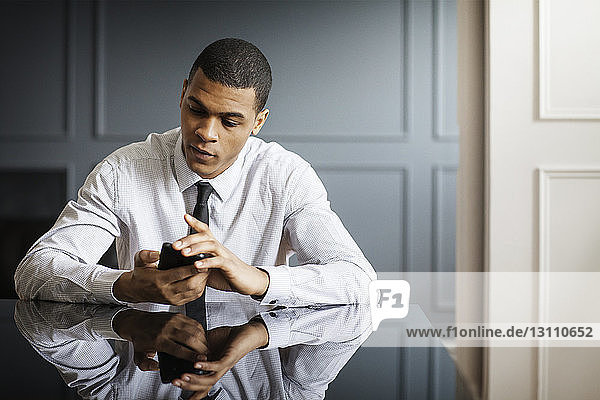 Geschäftsmann benutzt ein Smartphone  während er im Büro am Schreibtisch sitzt