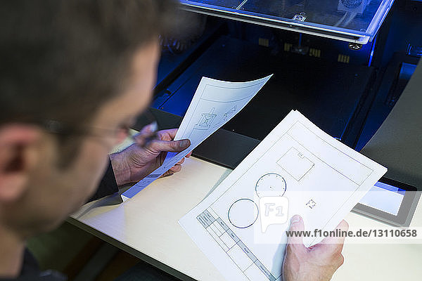 Ingenieur hält Dokumente per 3D-Drucker am Tisch im Büro