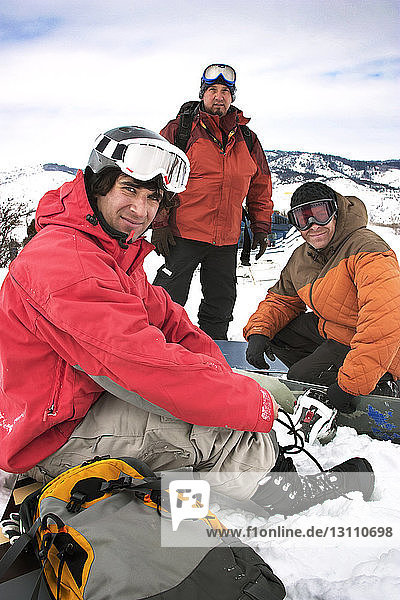 Smiling friends resting on snow covered mountains against sky