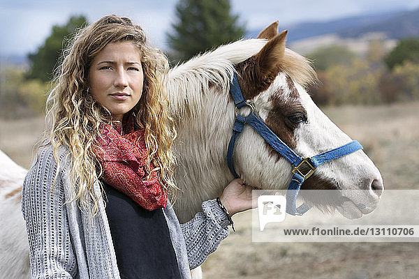 Porträt einer jungen Frau  die ein Pferd streichelt