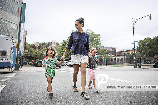 Girls eating ice creams while walking with mother on street