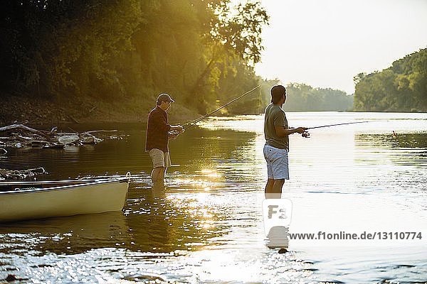 Freunde angeln  während sie bei Sonnenuntergang im See vor klarem Himmel stehen