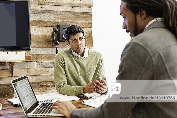 Geschäftsmann benutzt Laptop  während er mit einem Kollegen im Büro arbeitet