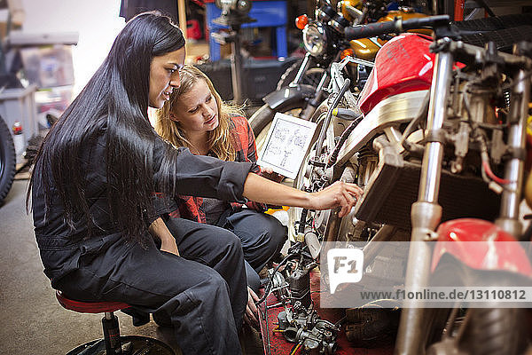 Female mechanics using digital tablet while repairing bike in workshop