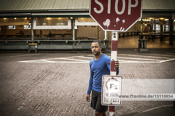 Porträt eines Athleten  der an einem Stoppschild auf der Strasse steht