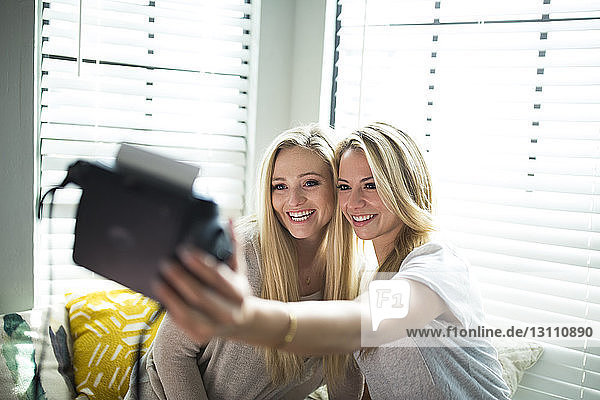 Lächelnde Freunde beim Selbermachen  während sie zu Hause auf einem Fensterplatz in einer Nische sitzen