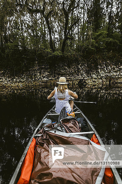 Rear view of young woman canoeing in lake at forest