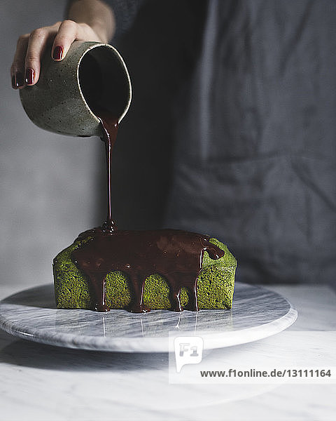Mitschnitt einer Frau  die Schokoladensoße auf Matcha-Pfund-Kuchen gießt