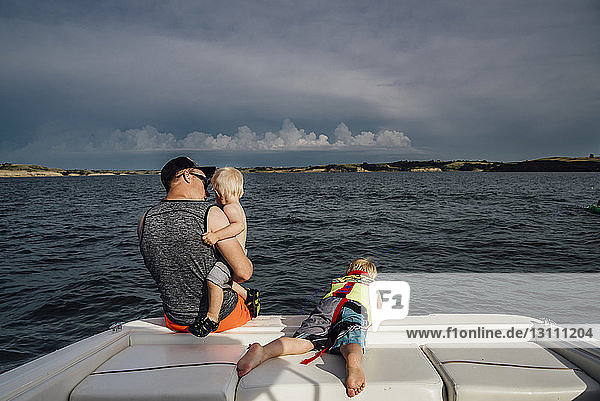 Rear view of father with sons traveling in boat on sea against cloudy sky