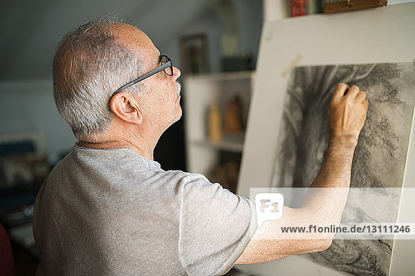 Konzentrierter älterer Mann  der zu Hause auf Leinwand skizziert