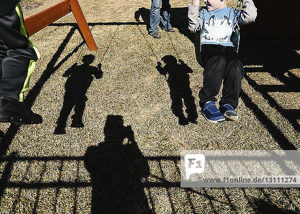 Schatten von Söhnen  die schwingen  während der Vater auf dem Spielplatz steht