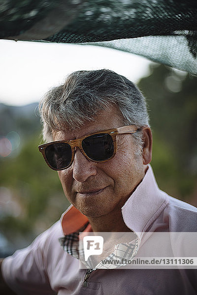 Close-up portrait of senior man wearing sunglasses while standing on building terrace during sunset
