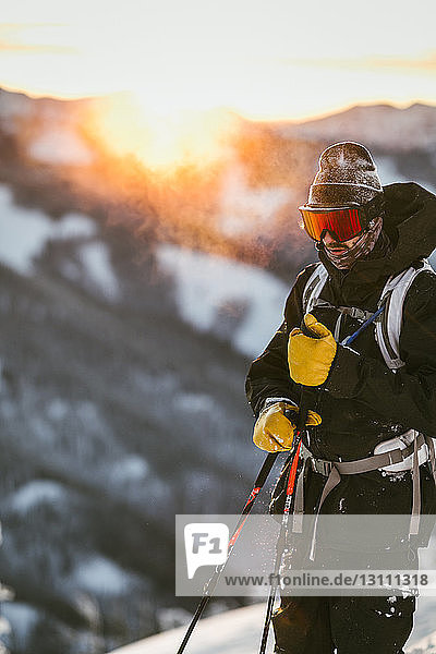 Man in ski-wear standing on snow covered mountain against sky during sunset