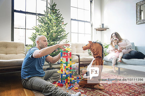 Vater spielt mit dem Sohn  während das Mädchen mit der schwangeren Frau zu Hause sitzt