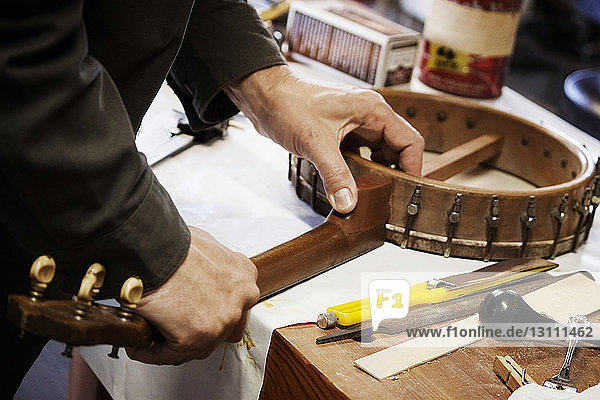 Beschnittenes Bild eines Menschen  der in einer Werkstatt Musikgeräte auf einem Tisch herstellt