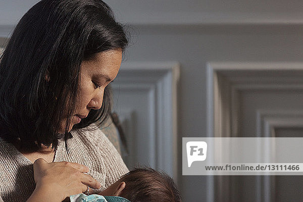 Close-up of mother breastfeeding daughter while sitting at home