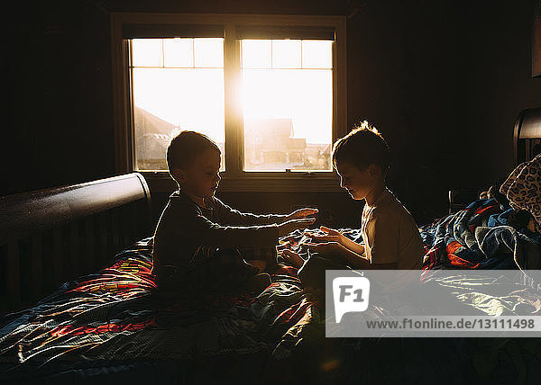 Brüder spielen im Bett sitzend am Fenster in der Dunkelkammer