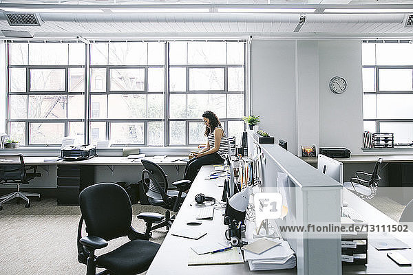 Seitenansicht einer Geschäftsfrau  die ein Mobiltelefon benutzt  während sie im Büro am Schreibtisch sitzt