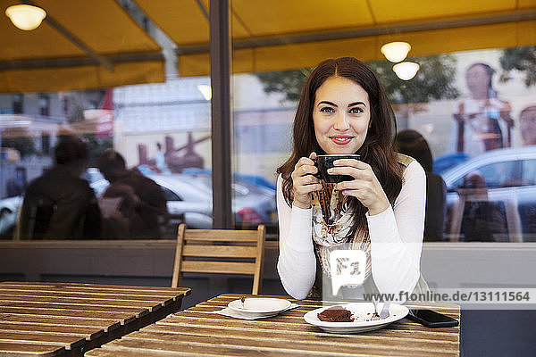 Portrait of woman holding coffee cup while sitting at sidewalk cafe