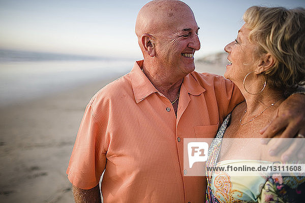 Glückliches älteres Ehepaar sieht sich an  während es am Meer gegen den Himmel steht