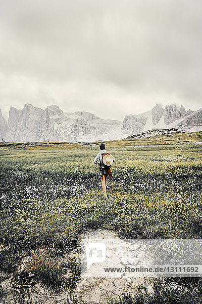 Rückansicht einer Wanderin mit Rucksack  die auf einem Grasfeld vor bewölktem Himmel steht