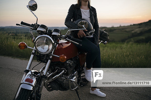 Low section of female biker sitting on motorcycle at country road