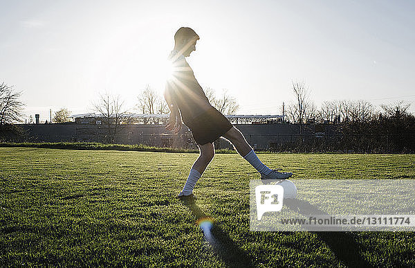 Man practicing soccer on grassy field against clear sky during sunset