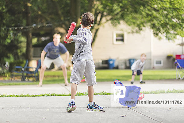 Rückansicht eines Jungen  der mit Vater und Bruder im Park Baseball spielt