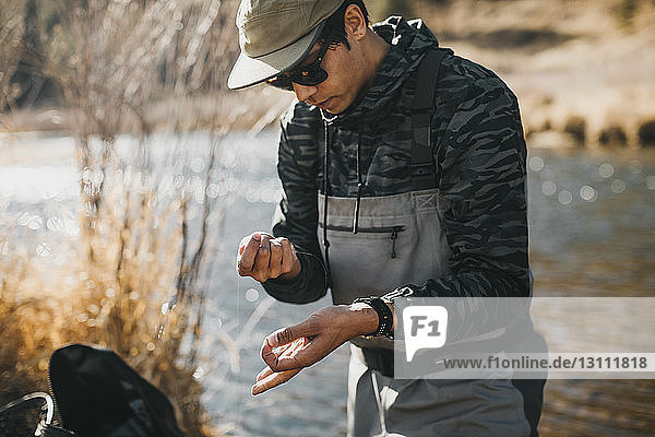 Male hiker holding fishing line while standing at riverbank
