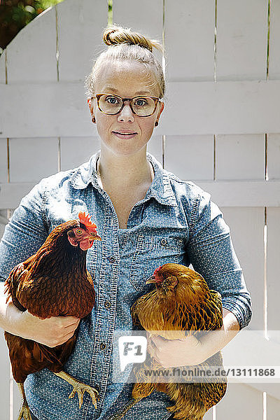Porträt einer Frau  die Hühner gegen eine Holztür hält