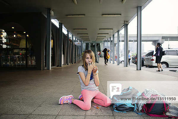 Girl drinking from water bottle while kneeling at sidewalk