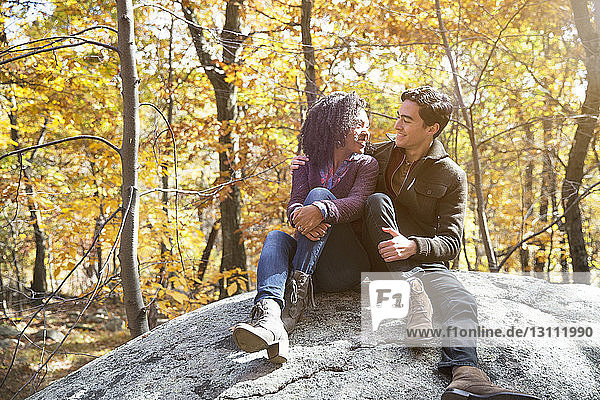 Loving couple looking at each other while sitting on rock in forest