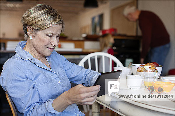 Frau benutzt Tablet-Computer  während der Ehemann mit der Enkelin im Hintergrund steht