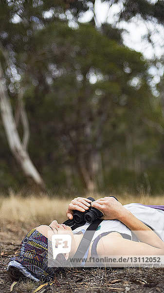 Woman holding binoculars while lying in forest