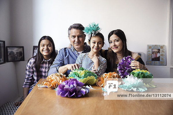 Portrait of family with paper flowers sitting at table against wall