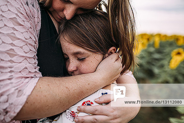 Nahaufnahme einer Mutter  die ihre Tochter umarmt  während sie in einer Sonnenblumenfarm steht