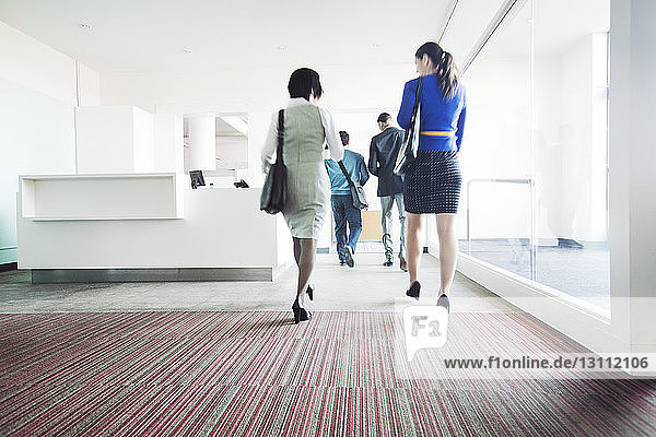 Rear view of business people walking on corridor by glass in office