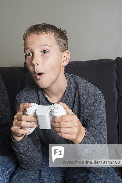 Junge spielt Videospiel  während er zu Hause auf dem Sofa im Wohnzimmer sitzt